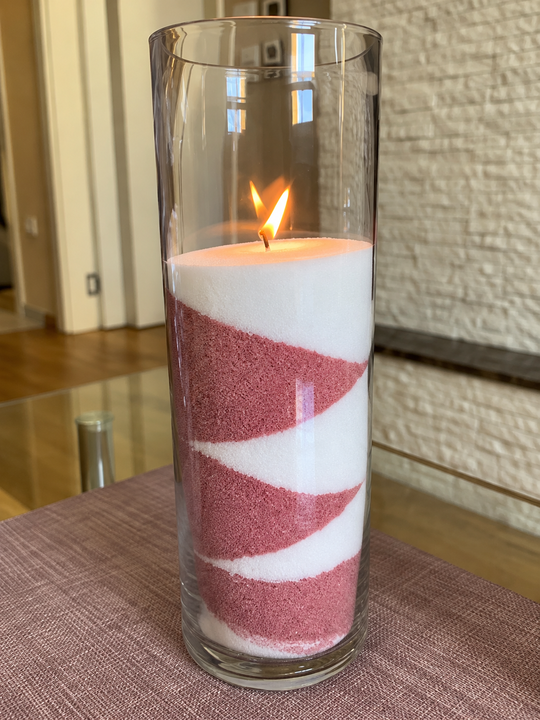 Cilindrična staklena vaza 30 × 10 cm sa roze-belim peščanim svećama i upaljenim fitiljem