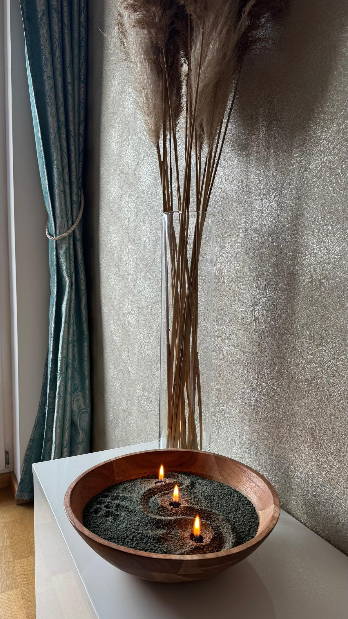 Velika tamnozelena peščana sveća u drvenoj činiji sa dekorativnim motivom i tri upaljena fitilja, Zest Candle.